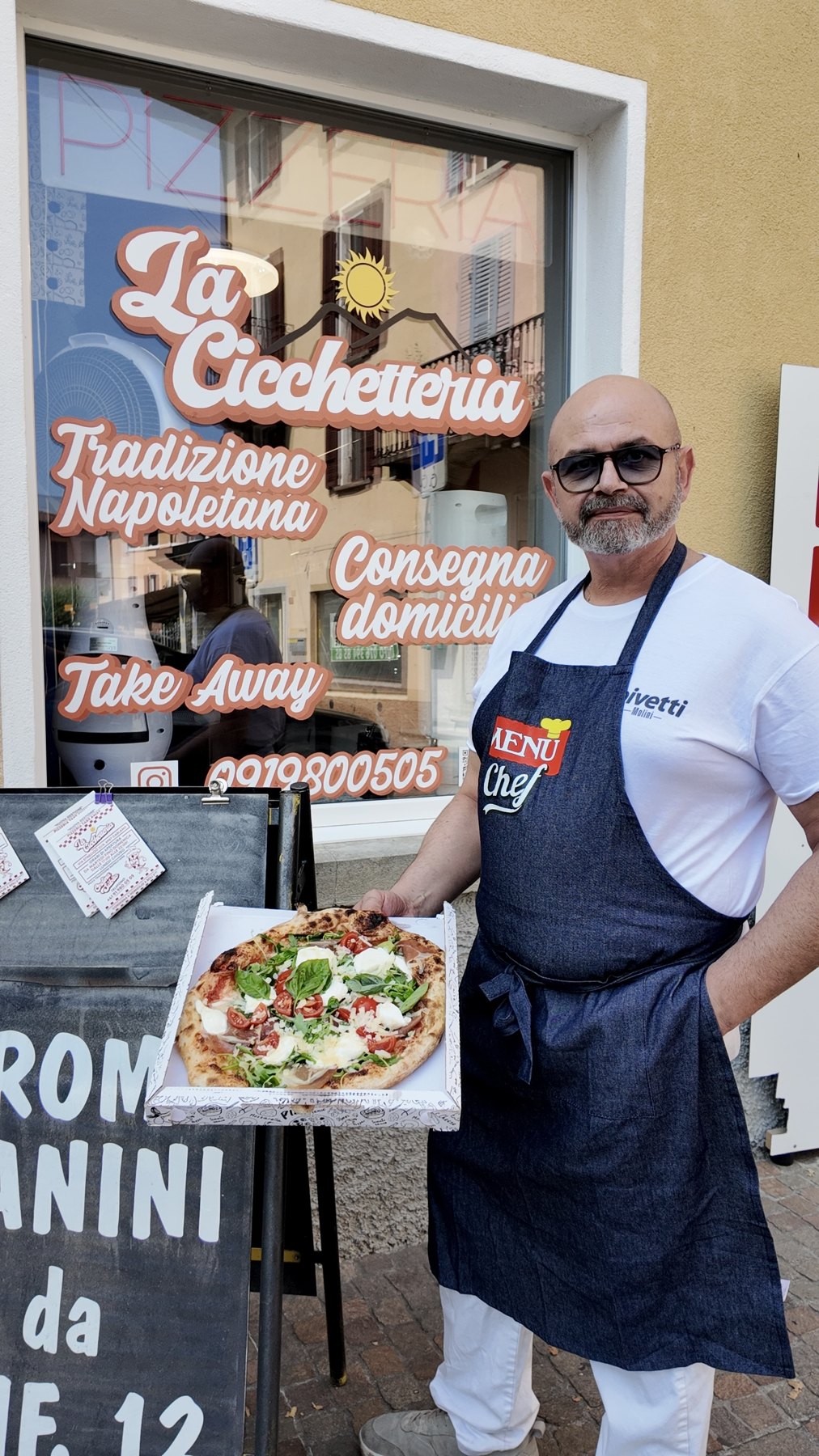 Enzo Ruocco, il proprietario, davanti alla vetrina de La Cicchetteria con una pizza in mano